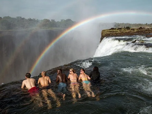 People resting in Devil's Pool at the edge of Victoria Falls with rainbow