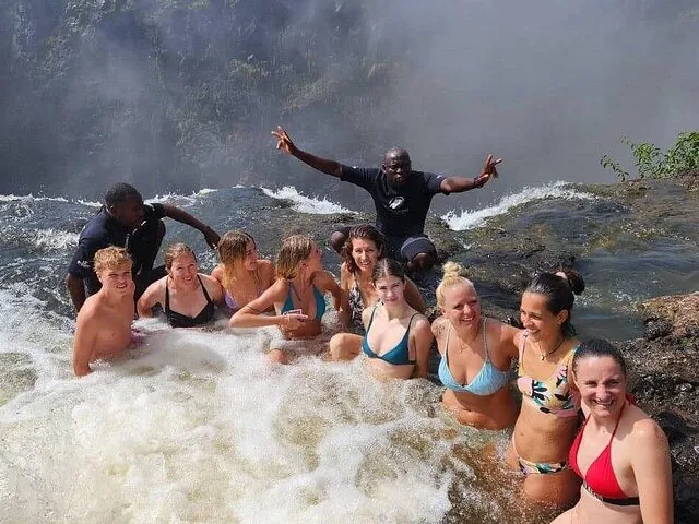 Large group of smiling friends enjoying the waters of Devil's Pool together