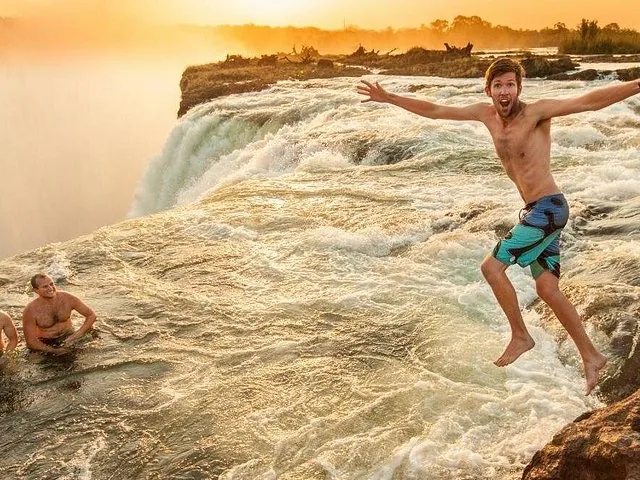 Two people posing on a rock next to the flowing waters of Victoria Falls