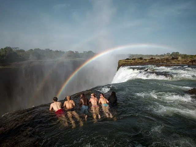 Group of tourists watching double rainbow from Devil's Pool at Victoria Falls