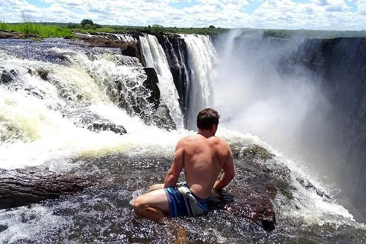 Man sitting near the edge of a roaring waterfall in bright sunlight