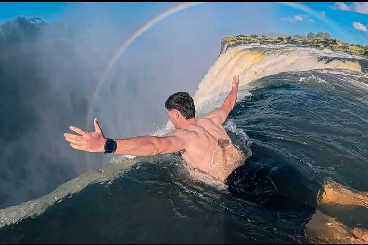 Man stretching his arms wide at the very edge of Devil's Pool with rainbow